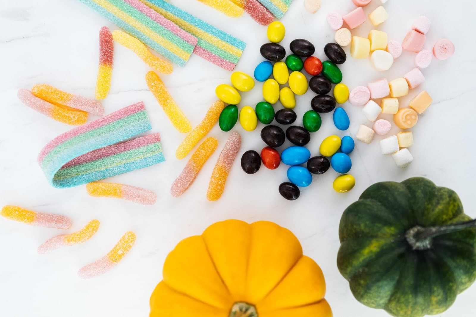 Vibrant assortment of Halloween candies and mini pumpkins, perfect for festive decoration.